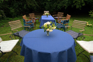 Set up for a family garden party with tables, blue tablecloths and different chairs on the lawn in a rural backyard