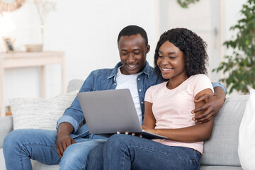 Smiling black couple using laptop at living room at home
