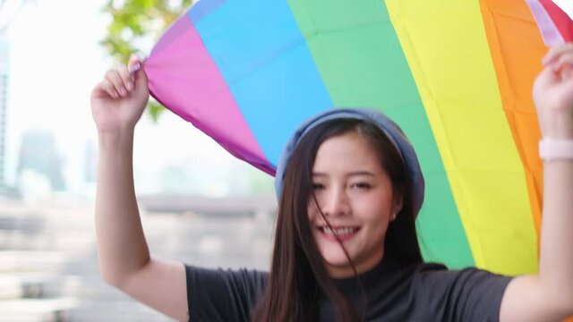Happy loving homosexual lesbian LGBT couple with rainbow flag at city streets at sunset. Portrait of happy lesbian LGBT woman wraped herself in rainbow flag. slow motion