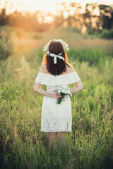 Caucasian happy girl in a white dress with a bouquet of flowers and a wreath in the summer