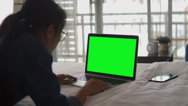 Over the shoulder shot of a business woman working in office interior on pc on desk, looking at green screen. Office person using laptop computer with laptop green screen