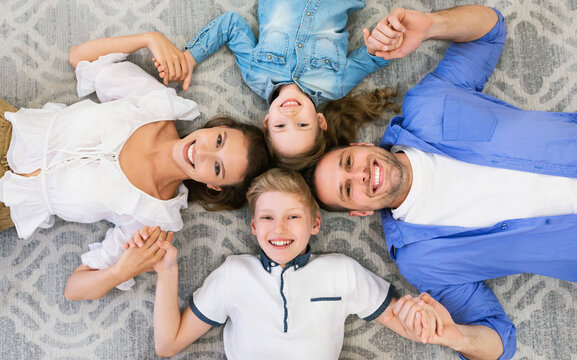 Family OPosing Lying On Floor Holding Hands Indoors, Top-View