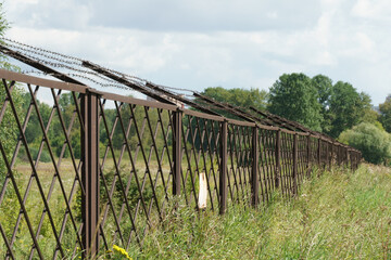 Old rusty fence with rusty barbed wire installed in the field and extending into the distance, warning sign