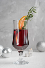 Glass of hot red mulled wine with orange slices and fresh rosemary usually prepared at christmas holidays in front of glowing silver candles on white wooden table. Vertical orientation