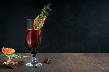 Glass of hot spiced red mulled wine usually prepared at cold winter holidays decorated with orange slices and rosemary in front of cinnamon bunch and anise. Image with copy space