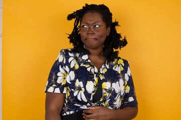 Photo of amazed puzzled young Caucasian female with ginger hair knot, curves lips and has worried look, sees something awful in front, isolated on white background, dressed in jean overalls.