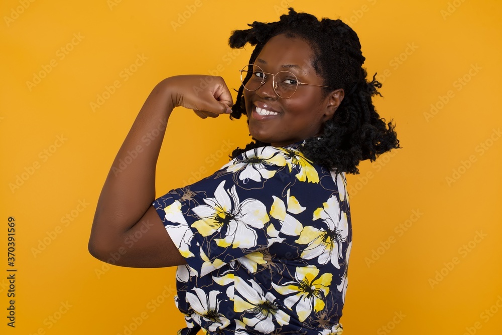 Wall mural Portrait of beautiful Caucasian woman isolated over yellow background,  showing muscles after workout. Health and strength concept.