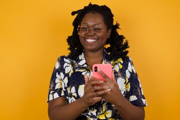 Pleased African American woman wearing casual clothes using self phone and looking and winking at...