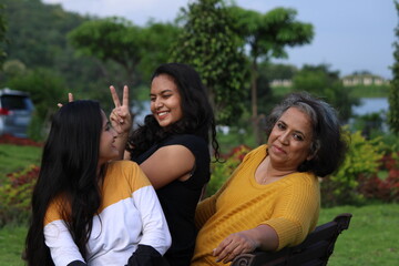 Happy looking Indian mother with her young daughters sitting on a gardens bench. Concept Mother's day