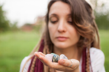 Young beautiful girl with long dreadlocks holds in hands 5 natural stones rose quarz, rhinestone,...