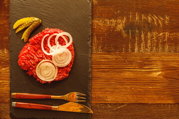 Minced meat cucumber sliced onion and cutlery on slate slab on wooden table