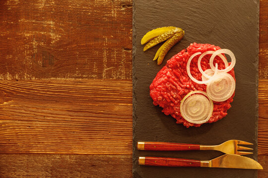 Minced meat cucumber sliced onion and cutlery on slate slab on wooden table