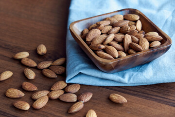 Almonds in small wooden bowl. Almonds laid freely on dark table. Row of bowls with almond nuts, top view. Peeled almond pattern