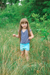 Little girl with long hair walks on the grass at the edge of the forest