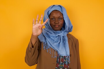 Young   woman standing against gray wall showing and pointing up with fingers number four while smiling confident and happy.