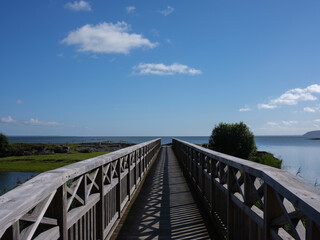 View of a wooden walkway leading to a small island. It is a perspective shot. There is a blue sky with som clouds. It is shot with a medium format camera.