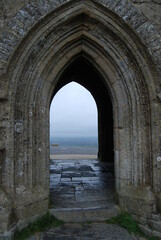 Fototapeta na wymiar Stone Archway Tunnel Opening of The Glastonbury Tor And Grey Walkway Path with Landscape View of Valley Below