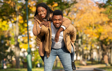 Fototapeta premium Happy black man carrying his girlfriend on back in autumn park