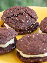 Chocolate and sesame yo-yo's chocolate biscuits or cookies on a yellow plate outdoors with soft green background
