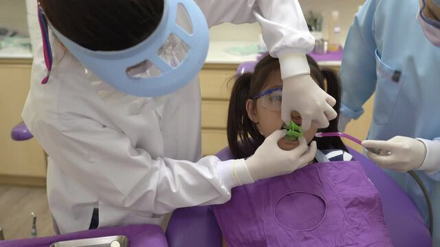 asian dentist doing fluoride treatment to young girl in dental clinic. dentistry and healthcare concept