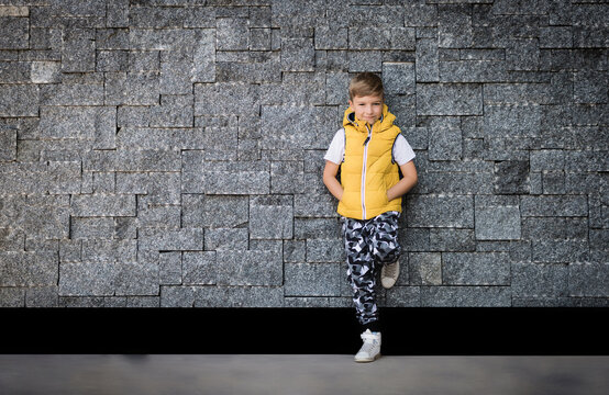 Cute Kid Leaning On Brick Wall And Looking At Camera.