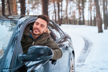 Young attractive Caucasian man sits at the wheel of his car sunny winter day.