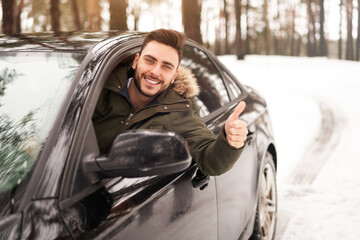 Young attractive Caucasian man sits at the wheel of his car sunny winter day.