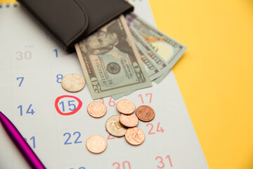 Wallet with money on a calendar on yellow background. Payment day.