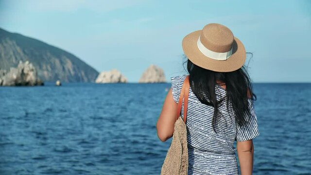 Relaxed girl in straw hat and sunglasses contemplate seascape at sunset. Shot with RED camera in 4K