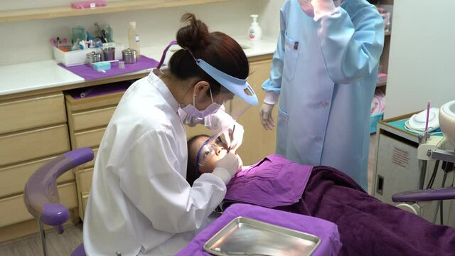 In dental clinic, asian dentist and assistant filling hole in tooth of young kid who has dental carrie and toothache. dentistry and healthcare concept