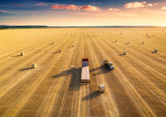 Aerial view of truck with hay bales. Agricultural machinery. Chamfered field and hay stacks after...