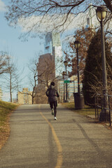 a man in a windbreaker and shorts runs in a park in winter in February near skyscrapers in...