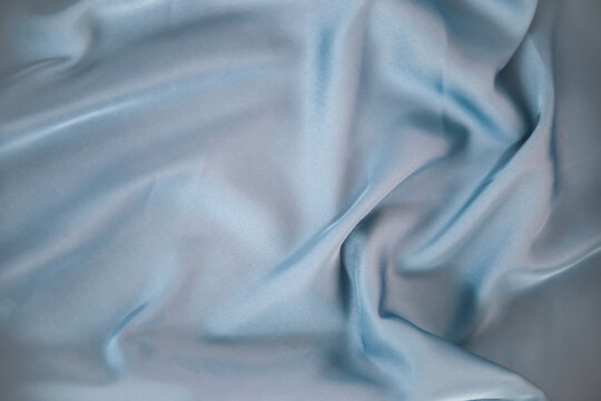 Close up picture of abstract silk fabric in light blue shade with waves to show the color as smooth textured background wallpaper of soft satin for fashion clothes in wedding industry with retro style