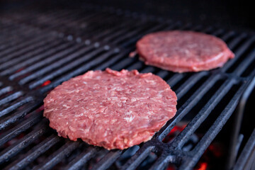 Raw beef burgers with a pinch of salt and black pepper on grill. prepared meat for grilling.Raw burger cutlets. Round patties of raw minced meat roasted on a metal grid.