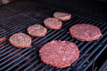 Raw beef burgers with a pinch of salt and black pepper on grill. prepared meat for grilling.Raw burger cutlets. Round patties of raw minced meat roasted on a metal grid.