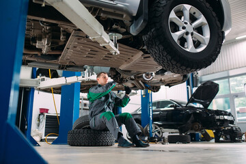 Car lifted in automobile service for fixing, worker repairs the wheel,