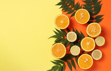 Composition of halves of lemons and oranges with green leaves on a bright yellow-orange background...