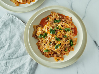 Pasta Farfalle with tomato sauce and ground meat in plate on white marble tabletop. Idea and recipes for easy, simple lunch or dinner one-pot meat goulash. Top down view or flat lay. Copy space