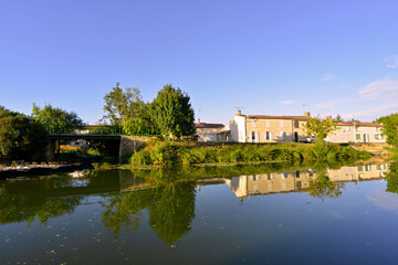 Fototapeta na wymiar Barques et reflets des maisons sur la Sèvre Niortaise à Damvix (85420), Vendée en Pays de la Loire, France