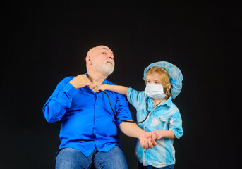 Stethoscope. Kid play doctor with granddad. Boy doctor playing with grandfather. Kid in doctor mask. Emergency. Treatment. Home treatment. Medicine. Doctor game.