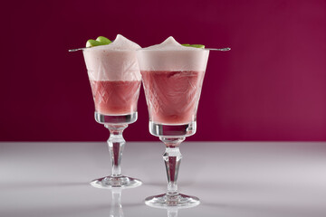 zwei pinke Cocktail Getränke mit grünen Apfel Spießen in alten Kristall Gläsern auf weißer reflektierender Oberfläche mit pinkem Hintergrund