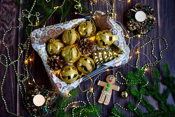 Christmas composition. Golden balls in a box, Christmas beads, garlands, candles in decorative candlesticks on a dark wooden background