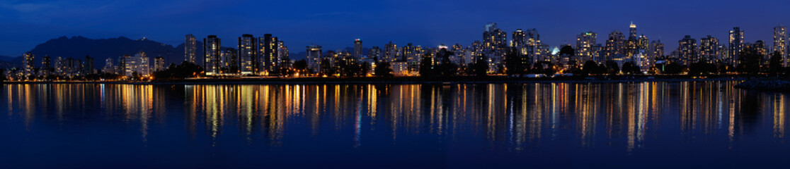 Fototapeta premium Wide Panorama of West End Vancouver skyline at dusk reflected in English Bay with Grouse Mountain