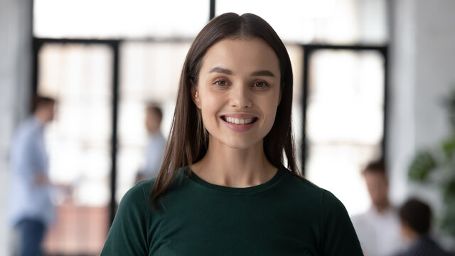 Head shot portrait close up smiling young beautiful businesswoman employee intern looking at camera, successful confident executive ceo manager standing in modern office, posing for photo