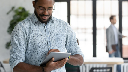 Close up focused African American businessman wearing glasses using computer tablet, standing in...