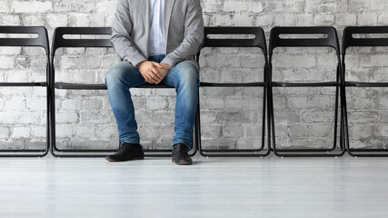 Cropped image closeup legs of confident man candidate waiting for job interview, searching work, businessman applicant sitting on chair in empty office hall, recruitment and employment concept