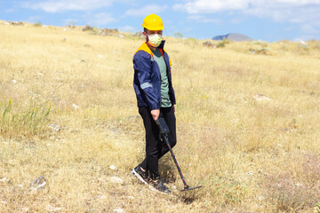 construction worker with metal detector in yellow helmet and medical mask working in the outdoor