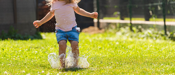 Happy child running through wet lawn splashinh water. Childhood concept