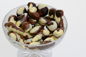 Belgian seashell shaped black white and milk chocolates in a chrystal bowl on white background