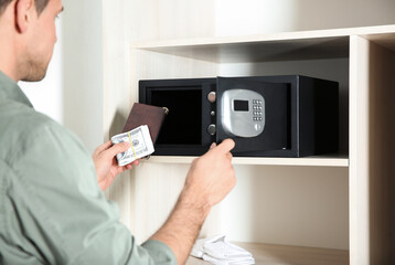 Man putting passport and money into steel safe, closeup